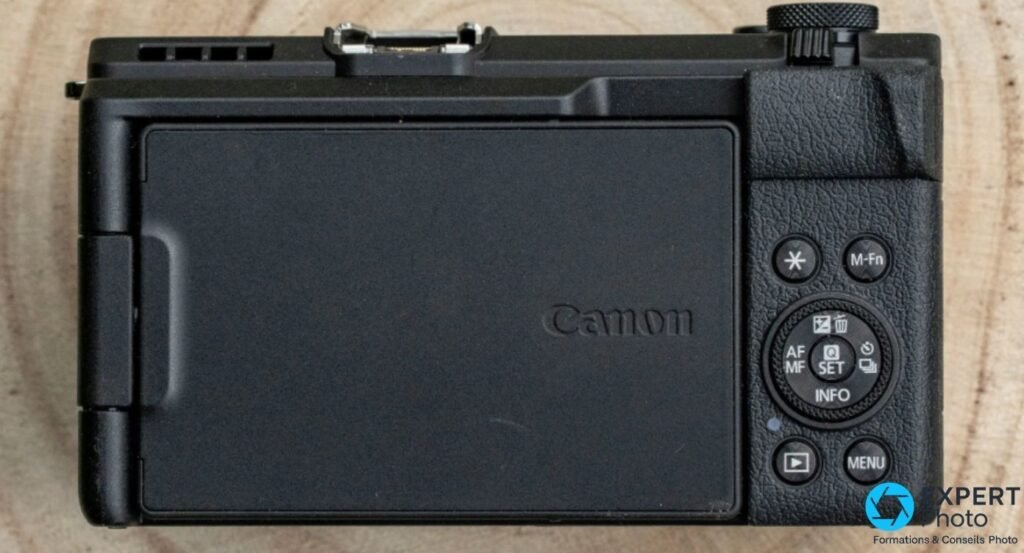 Canon PowerShot V1 vu de dos, écran rabattu contre le boîtier, boutons M-Fn, roue de commande et touche MENU visibles.
