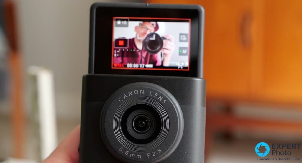 Canon PowerShot V10 vu en gros plan, écran inclinable affichant un photographe en cours de cadrage, indicateur REC visible.