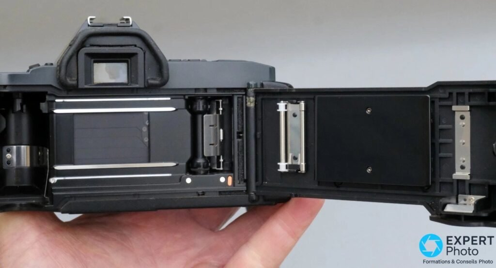 Canon T70 dos ouvert montrant la chambre du film, rideau d'obturateur, rails et bobine réceptrice motorisée. 