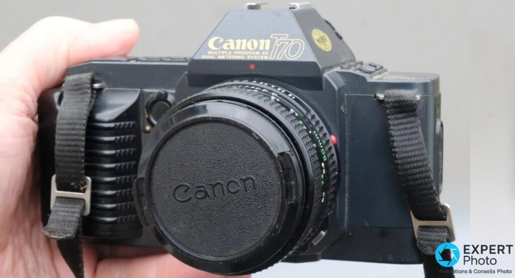 Canon T70 vu de face avec bouchon d'objectif Canon et étiquette dorée « PASSED » sur le pentaprisme. 
