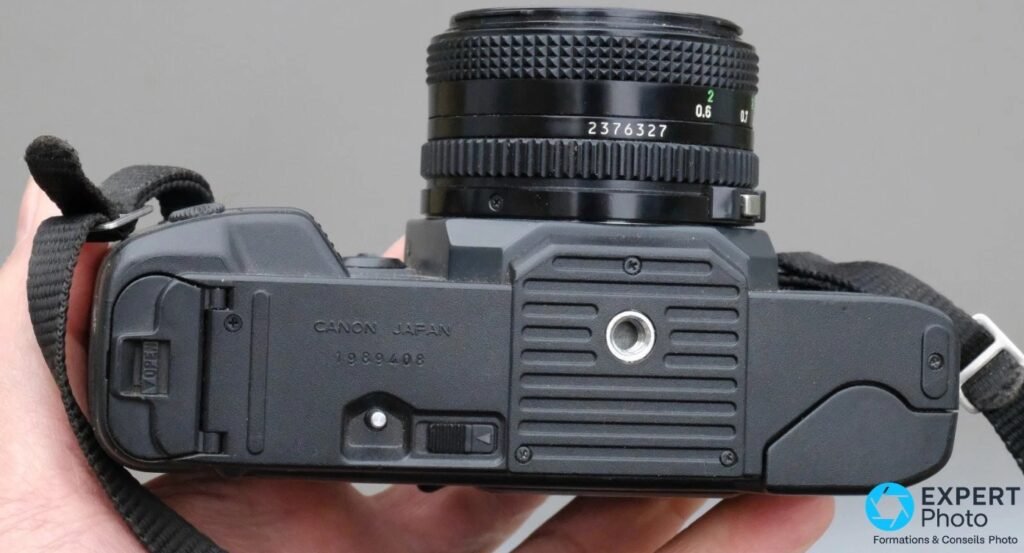 Canon T70 vu de dessous, semelle gravée « CANON JAPAN 1989408 », trappe à piles AA et filetage de trépied.