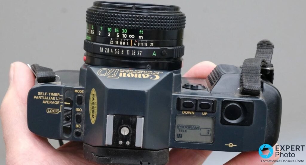  Canon T70 vu de dessus avec écran LCD affichant « PROGRAM TELE » et bague de diaphragme sur position « A ». 