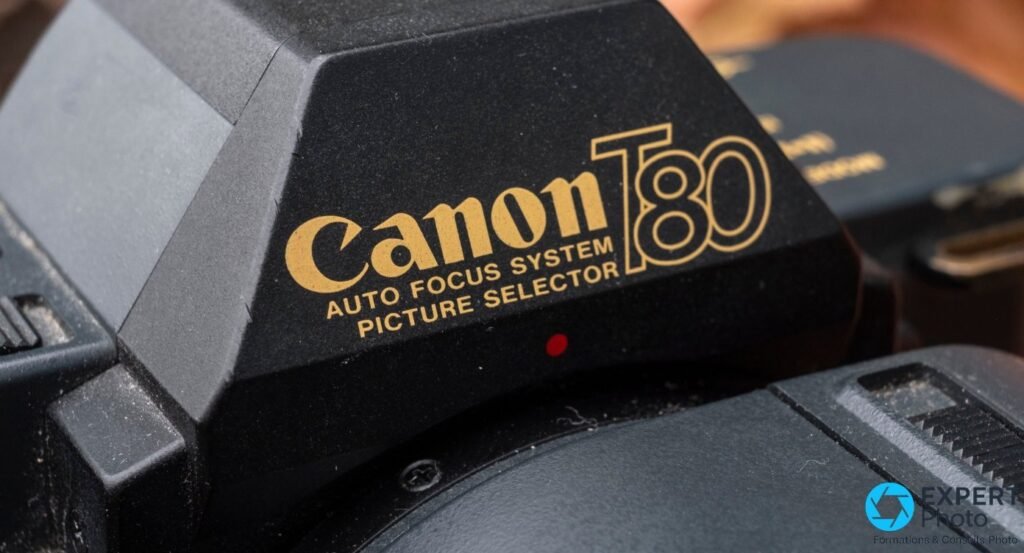 Canon T80, gros plan sur le logo doré Auto Focus System Picture Selector gravé sur le prisme du boîtier. 