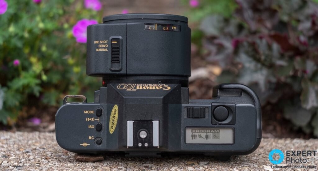 Canon T80 vu de dessus, contrôles MODE/ISO/BC, sélecteur AF, écran LCD PROGRAM avec pictogrammes. 