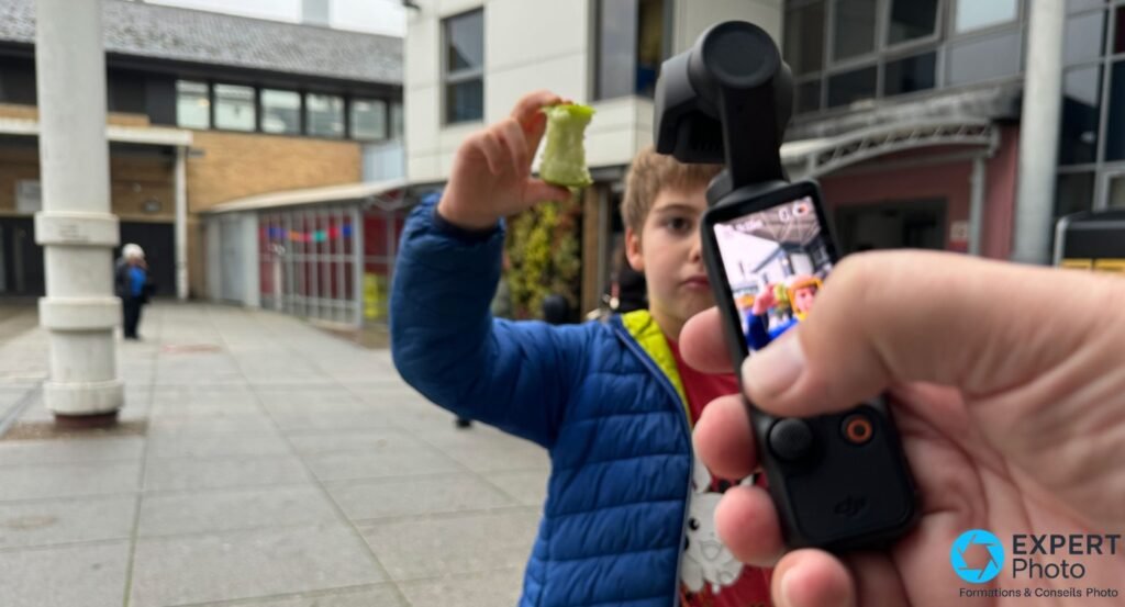 DJI Osmo Pocket 3 tenue en main en extérieur urbain, écran de prévisualisation visible, ActiveTrack en usage