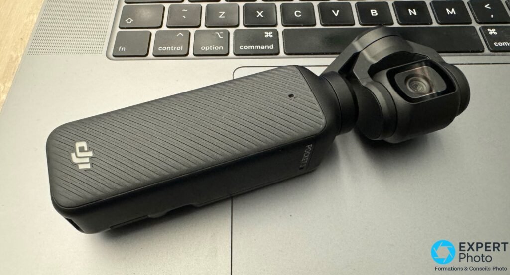 DJI Osmo Pocket 3 avec logo DJI posée sur un clavier MacBook, nacelle visible côté droit, vue 3/4 avant gauche