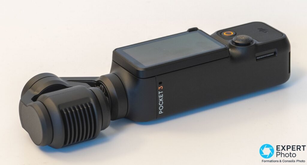 DJI Osmo Pocket 3 posée sur fond blanc, vue 3/4 avant gauche, bouchon objectif en place, écran éteint
