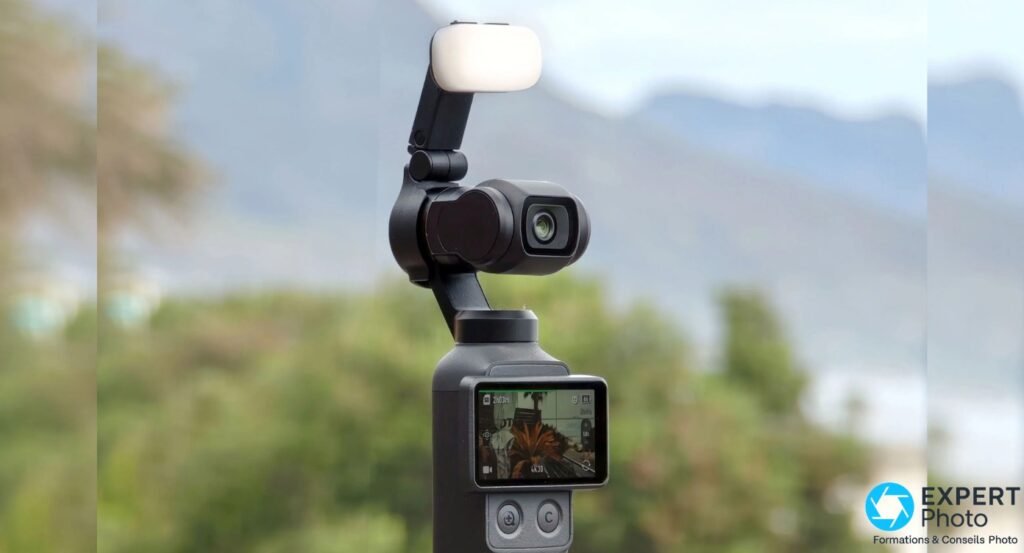 Caméra stabilisée DJI Osmo Pocket 4 noire avec bloc lumineux blanc sur la nacelle, écran allumé affichant 4K30, fond végétation flou