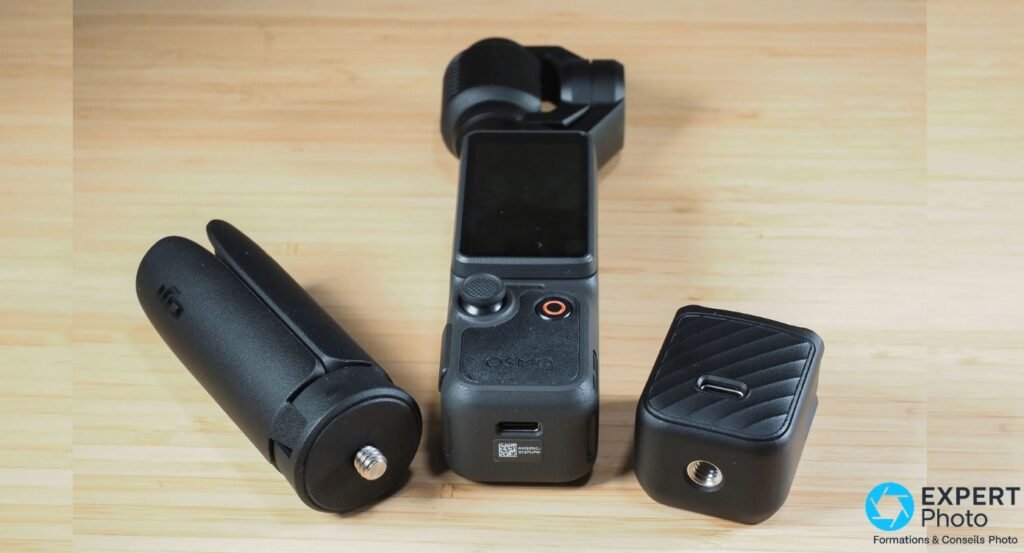 Caméra DJI Osmo Pocket avec marquage OSMO, posée avec deux accessoires noirs détachés sur surface en bois clair, vue de dessus