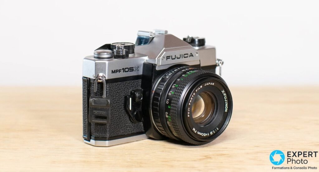 Fujica MPF 105X en 3/4 avant droit, bague de mise au point X-Fujinon 50 mm f/1.9 avec échelle de distances visible.