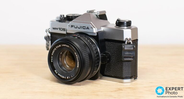 Fujica MPF 105X : reflex argentique d’initiation sur monture fermée Reflex argentique Fujica MPF 105X argenté et noir vu en 3/4 avant gauche, objectif X-Fujinon 50 mm f/1.9 monté, sur bois.