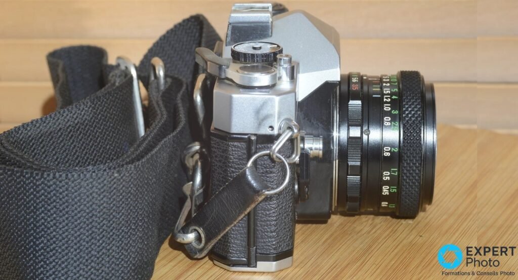 Fujica ST605N vu de profil, objectif et bague de diaphragme, sangle noire au premier plan sur table en bois