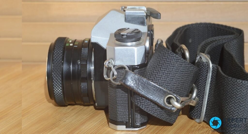 Fujica ST605N de 3/4 arriere, objectif a gauche et sangle textile enroulee a droite, sur fond bois clair