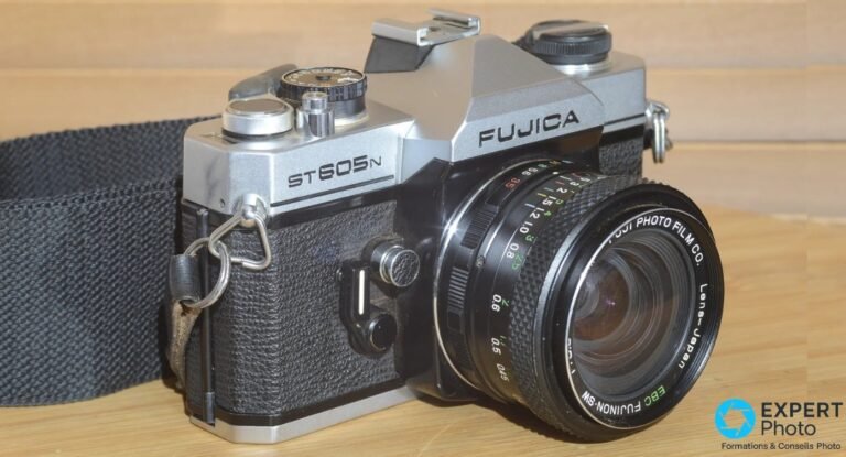 Fujica ST 605N : faut-il acheter ce reflex M42 d’occasion en 2026 ? Fujica ST605N argentique, vue 3/4 avant gauche avec objectif EBC Fujinon-SW et sangle noire, sur bois clair