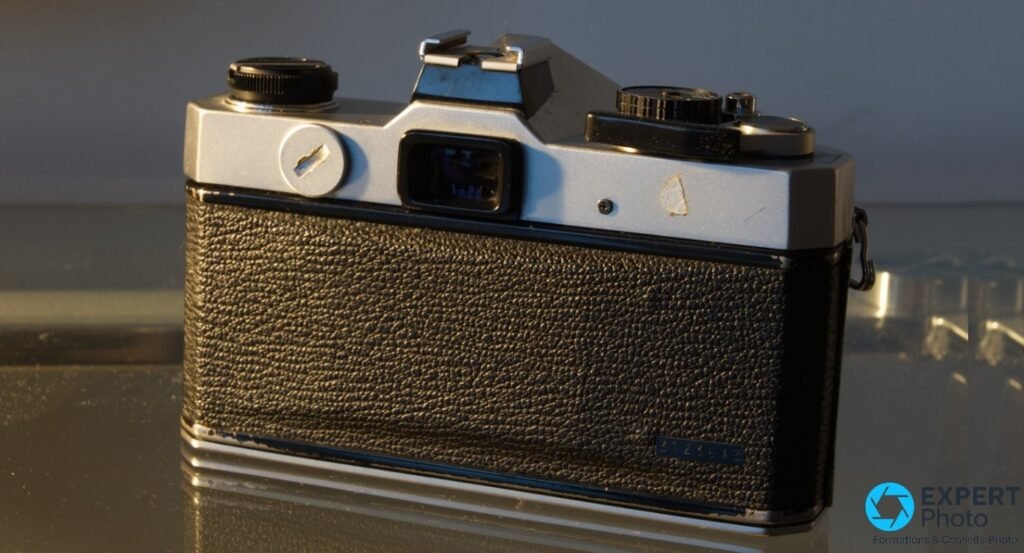Fujica ST605 vu de 3/4 arrière, dos en cuir noir grenu, viseur central et barillets visibles sur le capot chromé.