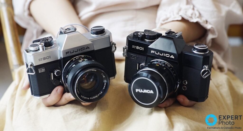Deux Fujica ST801 tenus en main, un argent avec objectif et un noir avec bouchon Fujica