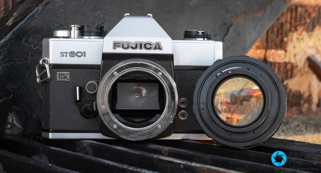 Boîtier Fujica ST801 ouvert sur la monture M42, objectif noir déposé à côté sur fond brique