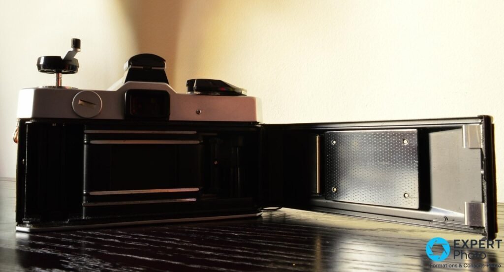 Fujica STX-1 dos ouvert : logement du film vide, rails et presseur visibles, volet rabattu vers la droite sur table foncée 