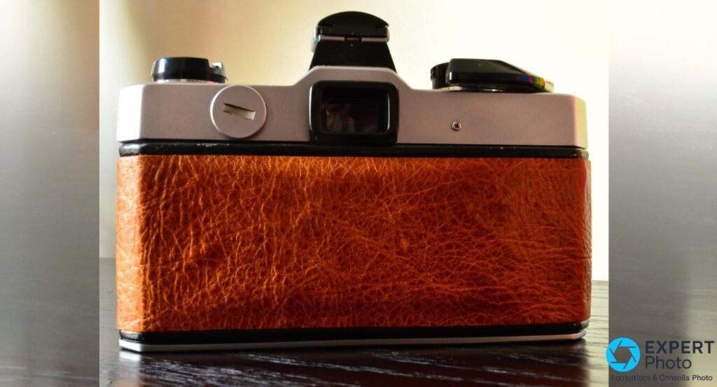 Dos du Fujica STX-1 fermé : oculaire de visée central, gainage cuir brun, capot argenté, posé sur une table foncée