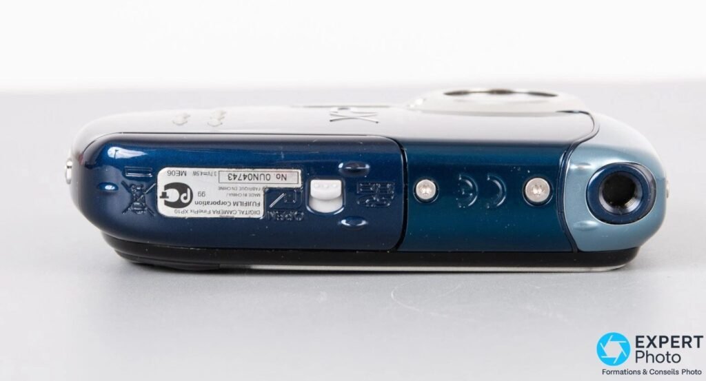 Fujifilm FinePix XP10 de dessous avec trappe batterie OPEN, étiquette DIGITAL CAMERA FinePix XP10 et filetage trépied