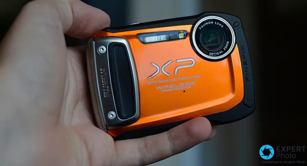 Fujifilm FinePix XP170 orange tenu dans une main droite, vue de face avec objectif Fujinon 5x WIDE.