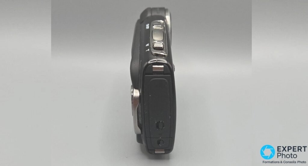 Fujifilm FinePix XP20 vu de profil : levier de zoom W/T en haut, déclencheur et trappe latérale verticale verrouillée.