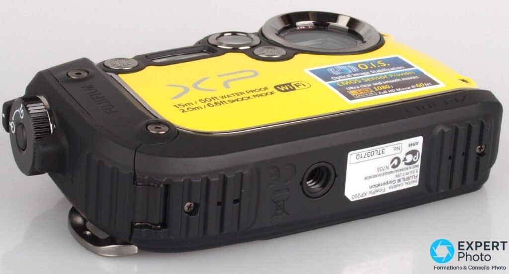 Fujifilm FinePix XP200 jaune vu de dessous en 3/4 arrière, étiquette de série et pas de vis trépied visibles.