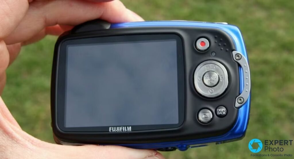 Dos du Fujifilm FinePix XP30 bleu et noir tenu en main, écran LCD éteint, croix MENU/OK et bouton DISP/BACK.