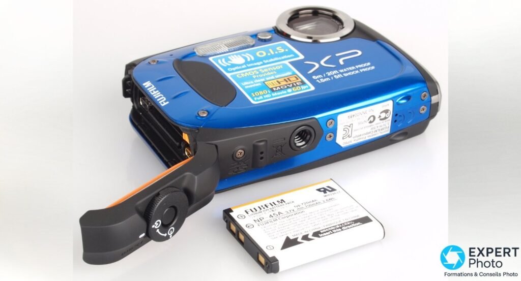 Fujifilm FinePix XP60 trappe batterie ouverte sur joint orange, batterie lithium-ion NP-45A posée à côté du boîtier. 