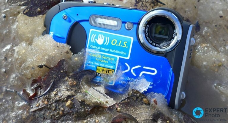 Fujifilm FinePix XP60 bleu posé dans un sol mouillé avec feuilles mortes et glace partielle, mise en scène extérieure.