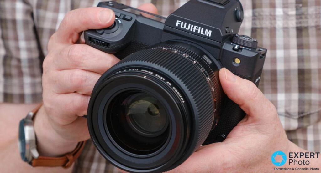 Fujifilm GFX100 II tenu a deux mains, objectif GF 55 mm monte, vue de face en situation
