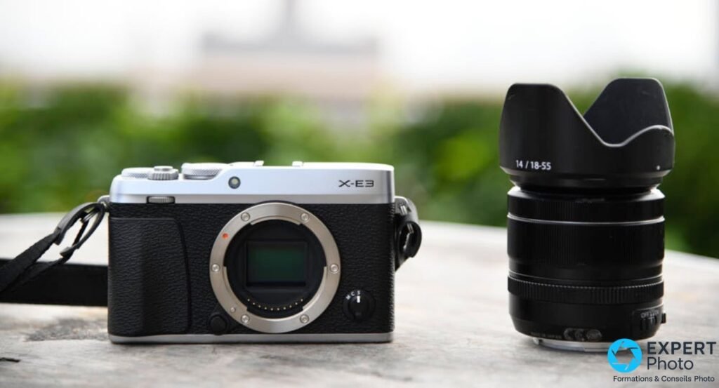 Boîtier Fujifilm X-E3 silver sans objectif, monture X et capteur APS-C exposés, à côté du zoom XF 18-55mm avec pare-soleil. 