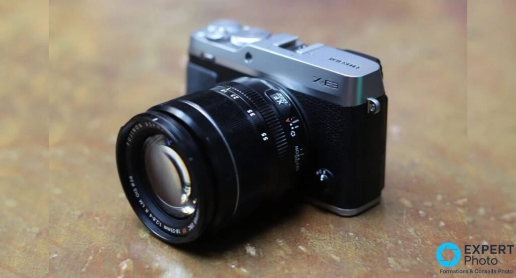Fujifilm X-E3 silver et noir équipé du zoom Fujinon XF 18-55mm f/2.8-4 R LM OIS noir, vue 3/4 avant droite sur fond marron.