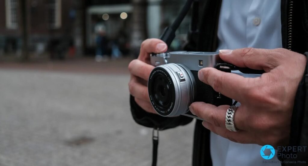 Fujifilm X-E5 silver tenu à deux mains par un photographe, place pavée en arrière-plan, photo de rue. 