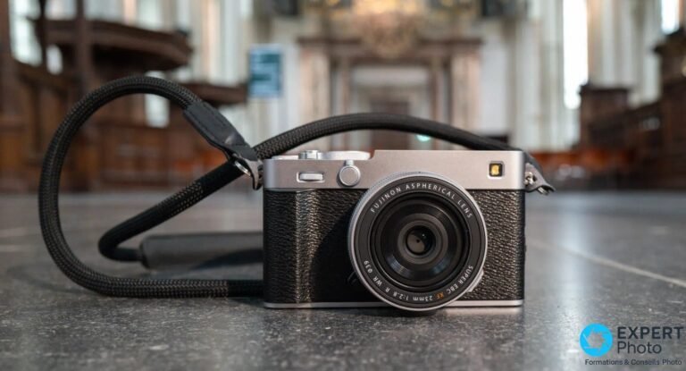 Fujifilm X-E5 silver posé sur sol gris, vue de face, sangle noire enroulée, objectif XF 23mm F2.8 monté.