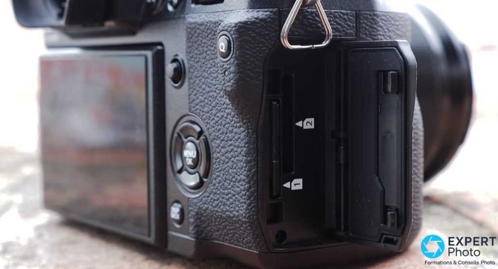 Trappe latérale du Fujifilm X-H1 ouverte sur les deux emplacements SD numérotés 1 et 2, avec écran arrière à gauche.