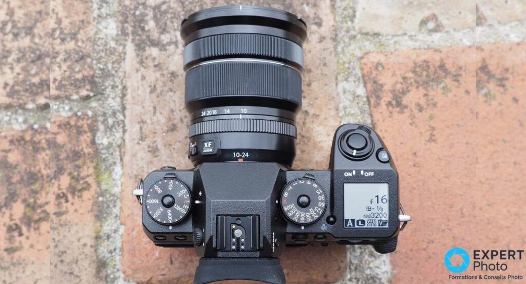 Vue de dessus du Fujifilm X-H1 montrant les molettes ISO et vitesse, l'écran LCD secondaire et l'objectif XF 10-24mm.