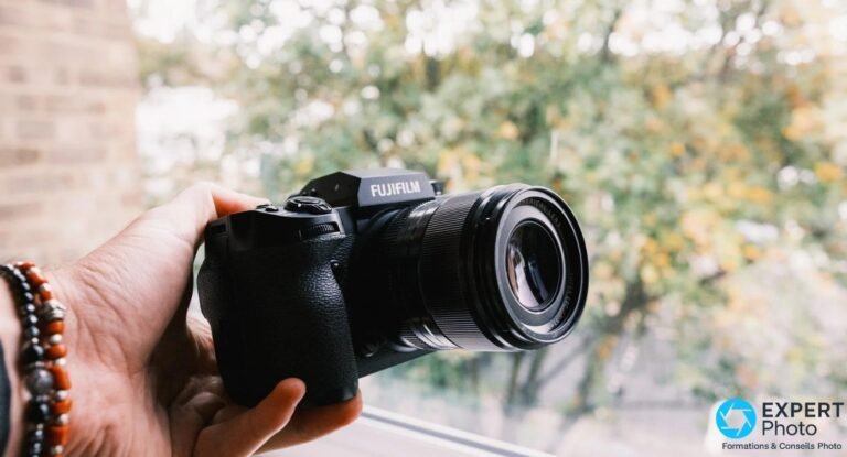 Fujifilm X-H2 équipé d'un objectif XF, vue de face en 3/4, tenu en main avec logo FUJIFILM lisible.