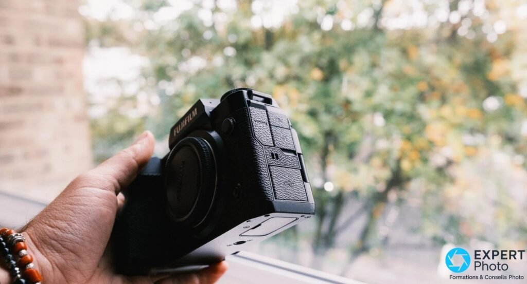Fujifilm X-H2 vu de profil 3/4, body cap monté, trappes de connexion latérales partiellement visibles.