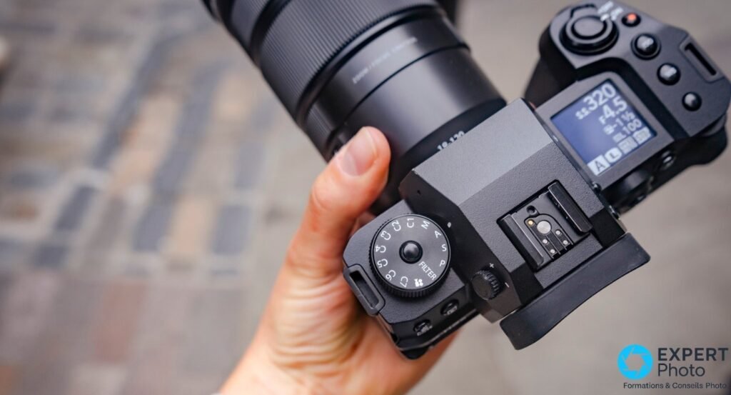 Vue de dessus du Fujifilm X-H2S en main, LCD supérieur, paramètres 1/320 s, f/4.5, ISO 100, molette des modes