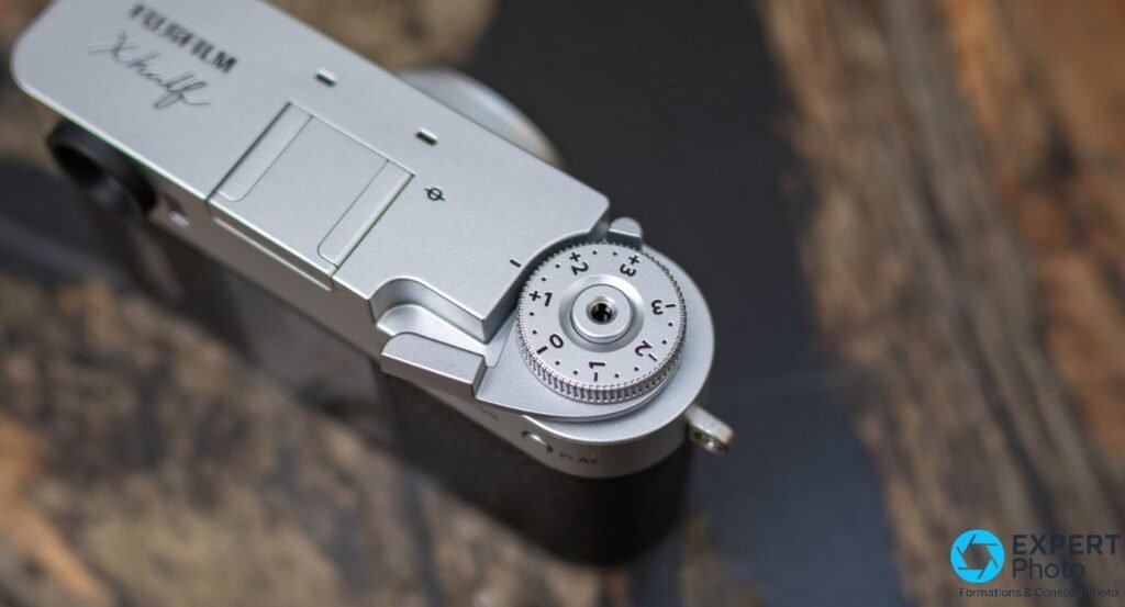 Vue de dessus du Fujifilm X Half : molette de correction d'exposition graduée et signature X half en cursive.