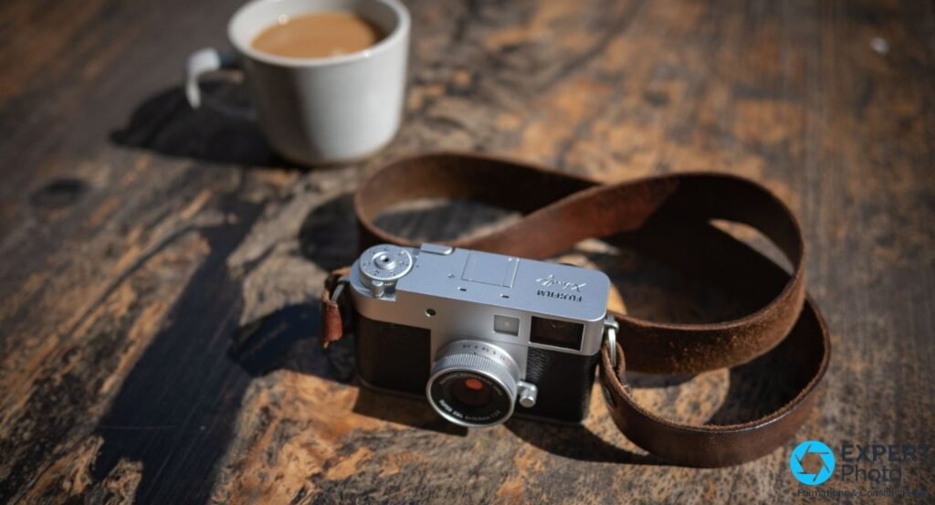 Fujifilm X Half argenté avec sangle en cuir marron sur table en bois rustique, tasse de café floue en arrière-plan.