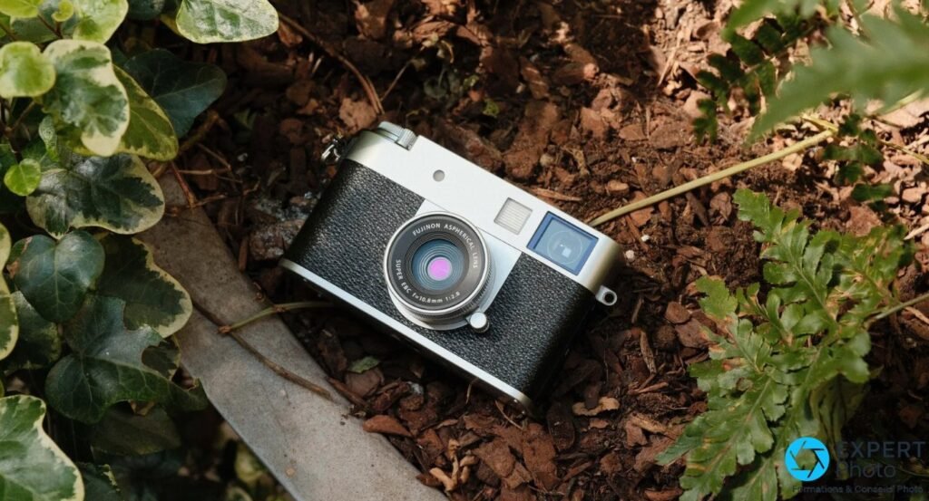 Fujifilm X Half argenté en vue trois quarts sur paillage d'écorce de jardin, lierre et fougère sur les côtés.