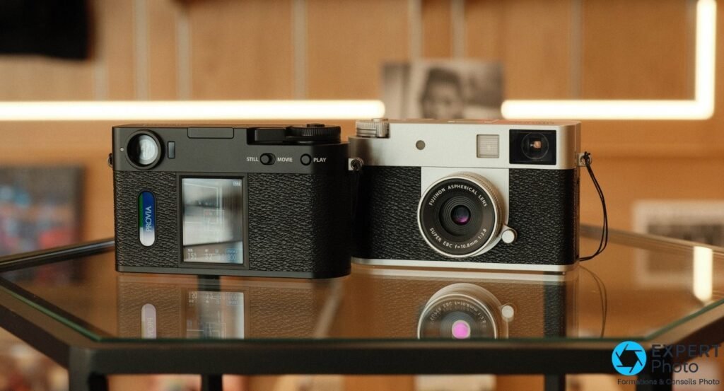 Fujifilm X Half en noir (vue arrière, écran PROVIA) et argenté (vue avant) côte à côte sur table en verre.