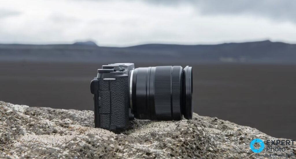 Fujifilm X-M1 noir vu de profil droit, objectif XC 16-50 mm monté, posé sur une roche, paysage flou en arrière-plan