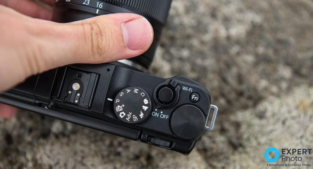 Vue de dessus du Fujifilm X-M1 montrant la molette PASM, le déclencheur, la griffe flash et les boutons Wi-Fi/Fn