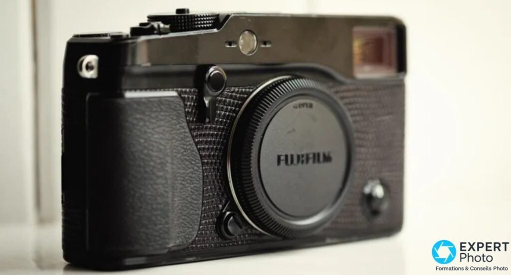 Fujifilm X-Pro1 noir vu de face avec bouchon de boîtier Fujifilm vissé sur la monture, fond clair flou