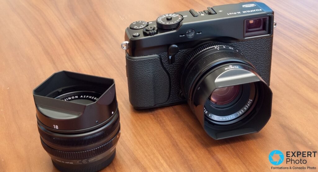  Fujifilm X-Pro1 noir avec Fujinon XF 35 mm f/1.4 monté, à côté d'un Fujinon XF 18 mm f/2 posé sur table bois