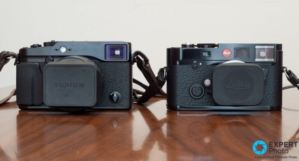  Fujifilm X-Pro1 noir avec bouchon Fujifilm posé à côté d'un boîtier télémétrique Leica M avec bouchon Leica