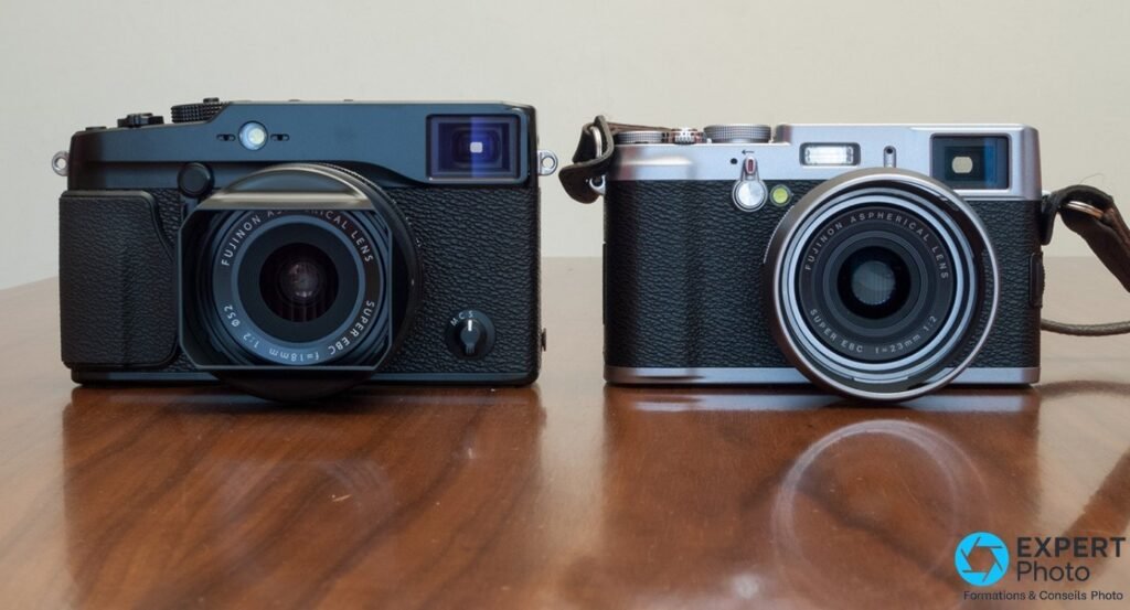  Fujifilm X-Pro1 noir avec objectif 18 mm f/2 et compact Fujifilm X100 argent posés côte à côte sur table bois 